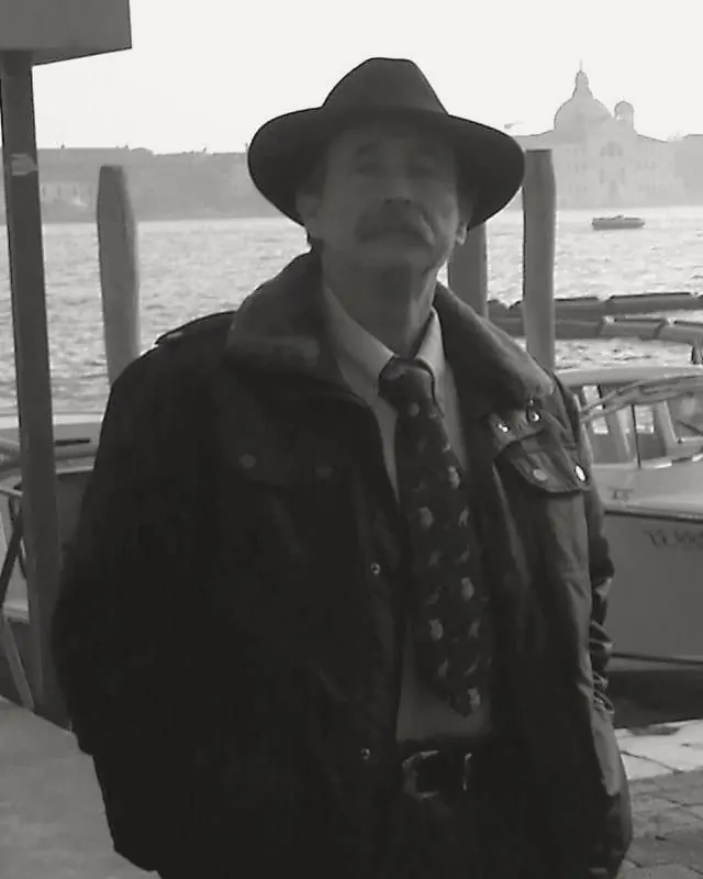 Archival photograph of Alfonso de Castro, Héctor's father, in a hat and coat on a quay in Venice, with the lagoon and a domed church behind