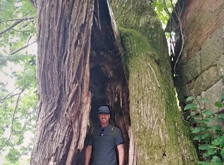 Héctor De Castro standing inside the hollow trunk of a thousand-year-old moss-covered tree in Galicia, Spain