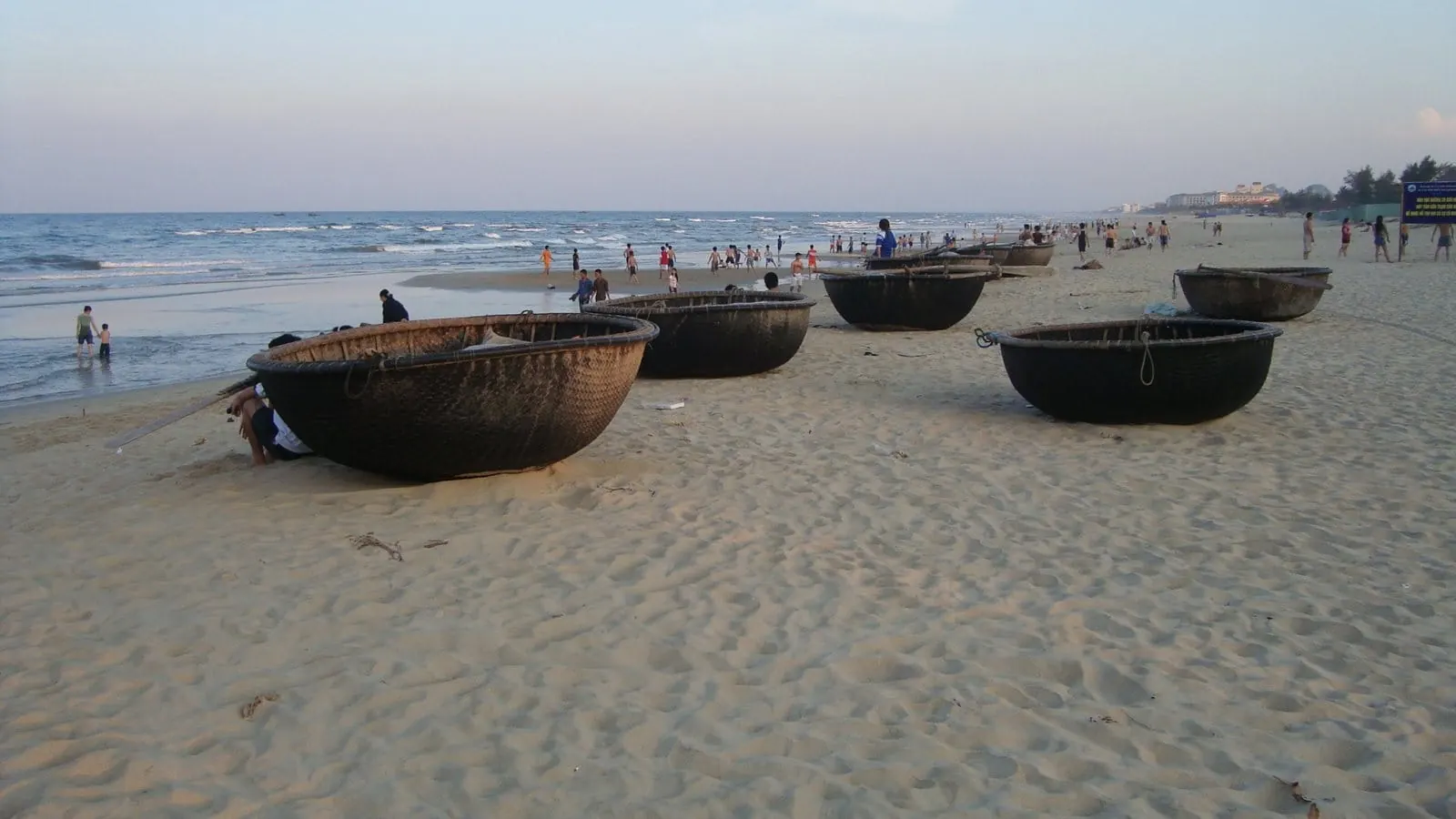 Round woven basket boats resting on the sand of a long beach at Da Nang, Vietnam, with swimmers and fishermen at the water's edge