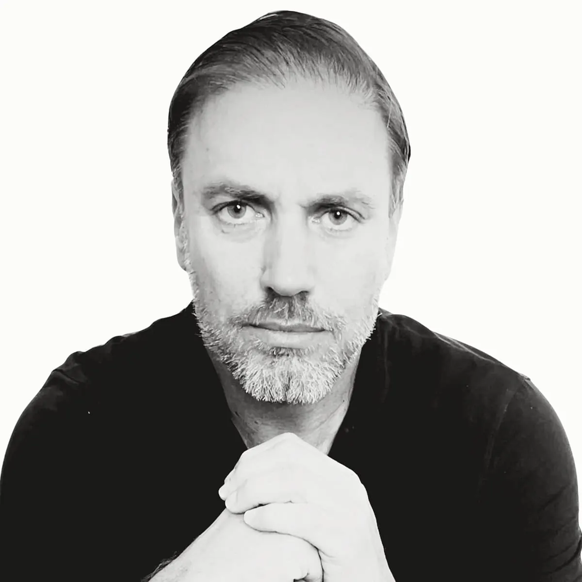 Black-and-white portrait of Héctor De Castro, hands clasped, looking directly at the camera