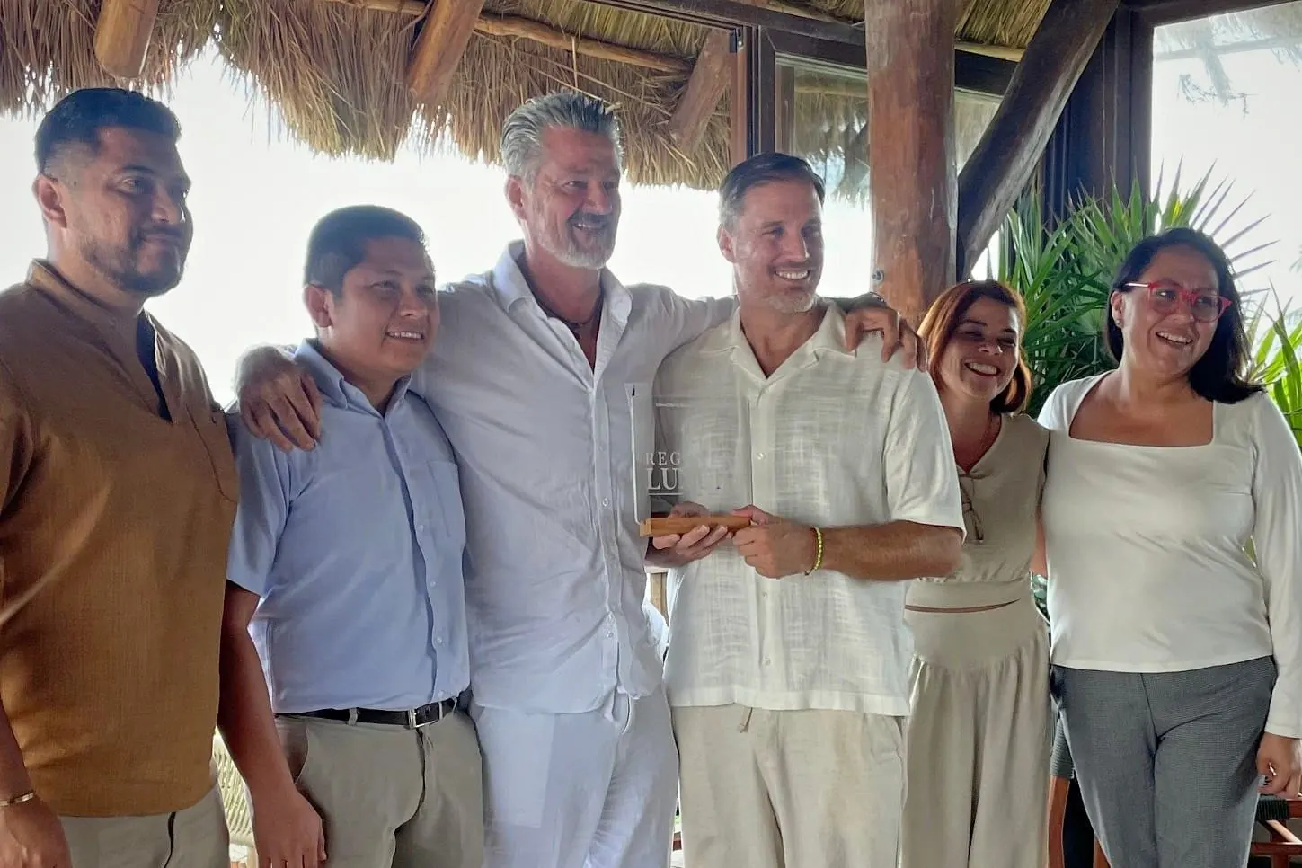 Héctor De Castro with the hotel team under a palapa, holding a Regenera Luxury distinction