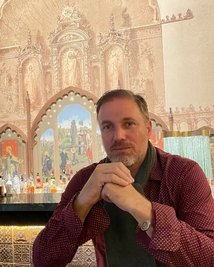 Héctor De Castro seated at a table in front of a mural of a Renaissance altarpiece at Hotel Palacio de Santa Paula, Granada